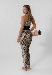 Aktivtøysett med leopardmønster laget av stretchy stoff, med halterneck-design og høy midje, holdt sammen med en oransje yogamatte.