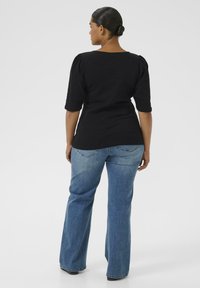 Sort ribbet top med trekvartærmer parret med lyseblå flared jeans. Toppen har en rund udskæring og samlinger ved skuldrene.