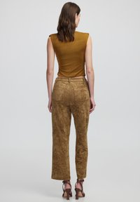 Pantalones marrones con textura y corte recto, complementados por una blusa sin mangas ajustada en mostaza. El diseño presenta una parte trasera sin costuras.