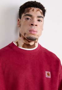Felpa rossa in cotone con scollo tondo e un'etichetta logo testurizzata sul lato sinistro del petto. Presenta una vestibilità rilassata e polsini a costine.