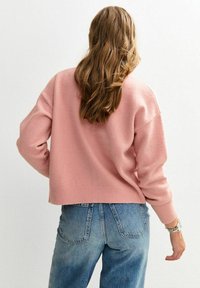 Suéter rosa, corto, de corte relajado, con textura de punto y puños de canalé, combinado con unos vaqueros de tiro alto, en un tono azul claro.