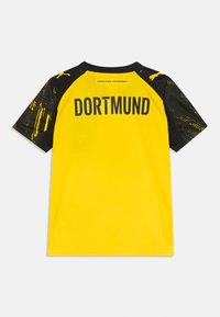 T-shirt jaune avec des manches noires, portant "DORTMUND" imprimé au dos. Les manches présentent un motif graphique texturé.