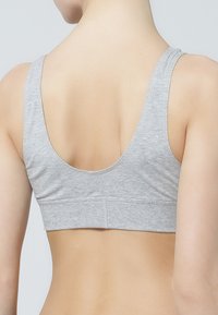 Grå bomullsbralette med låg scoop rygg, breda axelband och sömlös design. Texturen är slät med en mjuk finish.