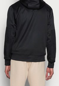 Zwarte hoodie met een gladde textuur, strakke manchetten en een capuchon. De achterkant heeft een minimalistisch ontwerp met paneelaccenten.