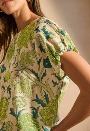 T-shirt ample en tissu léger avec des motifs floraux bleus et verts, à manches courtes et col rond, présentant des détails texturés.