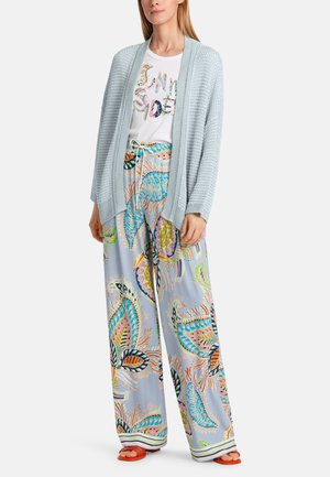Light blue knit cardigan over a white graphic t-shirt and colorful, patterned wide-leg pants featuring fish and floral designs. Orange slides.