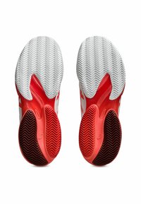 Des chaussures de sport rouges et blanches avec une semelle en caoutchouc texturée présentant des motifs en chevrons et des découpes pour plus de flexibilité.