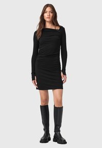 Vestito nero a maniche lunghe con scollatura quadrata, lati arricciati e silhouette aderente, abbinato a stivali neri al ginocchio.