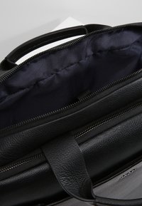 Svart läderväska med dragkedjestängning, som har en texturerad yta och ett rymligt mörkblått innerfoder. Handtag är fästa på toppen.