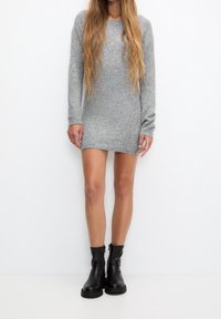 Robe pull grise en tricot à manches longues et coupe décontractée, assortie à des bottines noires à fermeture éclair et à semelle texturée.