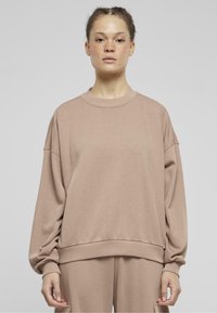 Felpa oversize marrone realizzata in materiale morbido, con scollatura rotonda, spalle cadute e orlo a coste ampie.