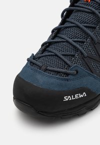 Niebieski but sportowy z teksturowaną cholewką z tkaniny i zamszowymi akcentami. Posiada czarną gumową podeszwę oraz białe logo "SALEWA" po bokach.