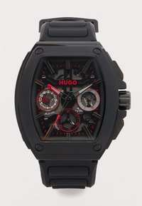 Μαύρο ρολόι χειρός Hugo με ορθογώνιο καντράν, κόκκινες λεπτομέρειες, τρεις υποδιακόπτες που δείχνουν 24ωρο, ημέρα και ημερομηνία, και μαύρο λουράκι από σιλικόνη.