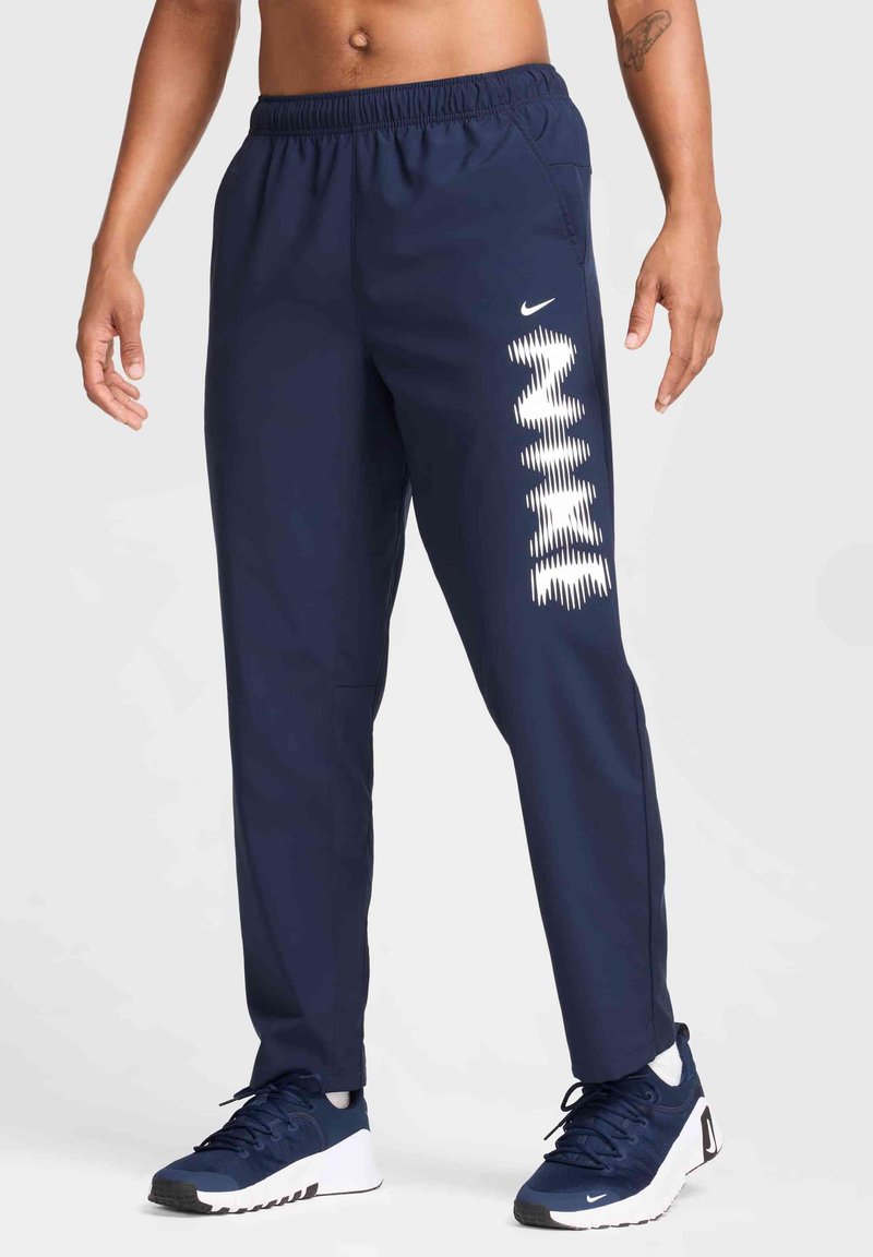 Marineblå sportsbukser med elastisk talje, sidelommer og hvidt Nike-logo-design på venstre ben. Egnede til sport og afslappet brug.