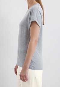 Jasnoszary t-shirt z krótkim rękawem o luźnym kroju i dekolcie w serek, wykonany z miękkiej, teksturowanej tkaniny, w połączeniu z jasnymi spodniami.