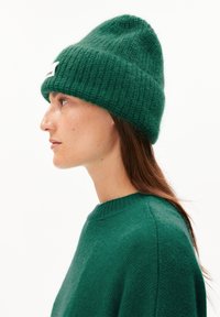 Groene gebreide beanie met een geribbeld patroon en een opgerolde rand, gecombineerd met een bijpassende groene trui met een ronde halslijn.