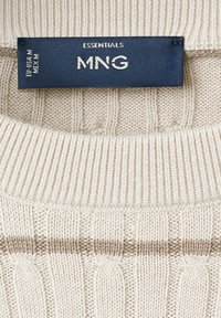 Pull en maille couleur crème avec col côtelé et bande horizontale marron sous l'encolure, avec une étiquette de taille MNG Essentials bleu foncé.
