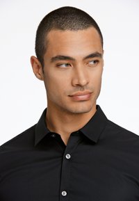 Zwarte button-up shirt met een puntige kraag; gladde stoftextuur; voorzien van lichtgrijze knopen en een getailleerd ontwerp.