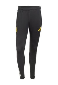 Svarta sportbyxor med elastisk midjeband, med gula logotyper från Real Madrid och Adidas, samt vita ränder längs sidorna.