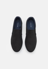 Black slip-on shoes with a canvas upper, white rubber sole, and a blue inner lining. No visible hardware or patterns. Simple, streamlined design.