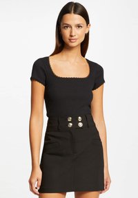 Black ribbed top with a square neckline and lace trim paired with a high-waisted black skirt featuring gold button accents and front pockets.