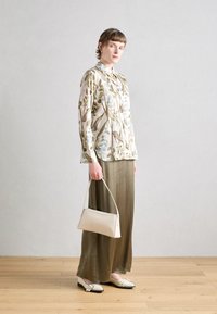 Blusa con motivo floreale in tessuto leggero, gonna verde oliva, borsa beige e ballerine color crema con dettagli neri. Design elegante a maniche lunghe.