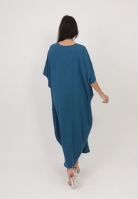 Robe kaftan fluide en teal avec des manches chauve-souris, un col rond et une silhouette ample, fabriquée en tissu léger et texturé.