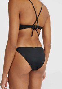 Set di bikini neri con schiena incrociata, spalline regolabili, fiocchi laterali sui pantaloni, texture liscia e dettagli hardware minimi.