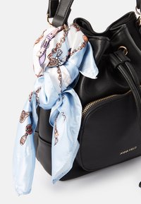 Schwarze Leder-Einkaufstasche mit weicher Textur, goldfarbenem Reißverschluss und einem blauen, gemusterten Seidenschal, der am Griff gebunden ist. Markenname sichtbar.