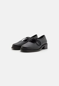 Black leather shoes with a rounded toe, lace detailing, and a low block heel. Smooth texture and minimalist design.