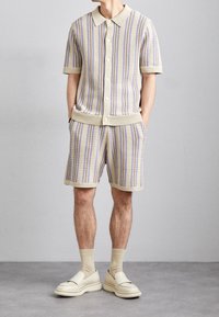 Gebreide tweedelige set met een kortärmelig top met knopen en bijpassende shorts. Lichtbeige met blauwe en paarse strepen en geribbelde accenten.