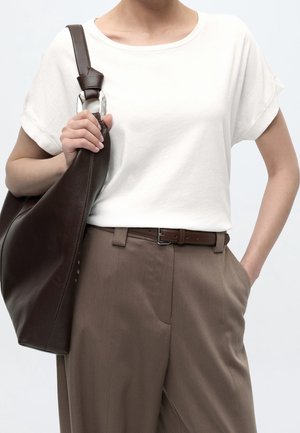 Person trägt ein weißes kurzärmeliges Hemd und braune Hose mit Gürtel, trägt eine große dunkelbraune Lederschultertasche.