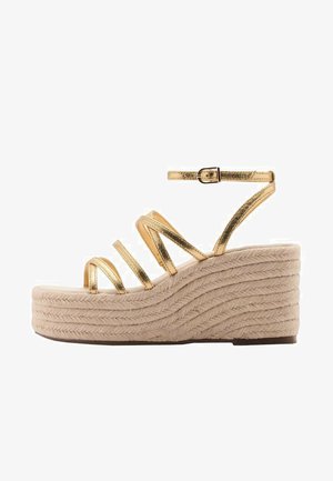 Gyldne metalliske stroppede kilehæle med en tykk vævet beige platformheel, udstyret med en spændejustering og en struktureret overflade.