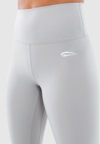 Jasnoszare legginsy z wysokim stanem, wykonane z gładkiej, elastycznej tkaniny, z małym białym logo po boku i bezszwowym wykończeniem.