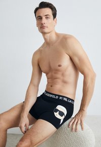 Crne bokserice s prilagođenim dizajnom, elastičnim pojasom s logotipom "KARL LAGERFELD" i grafikom lica s naočalama na prednjoj strani.