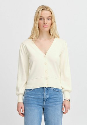 Cream-colored cardigan with a v-neck, button front, ribbed hem, and balloon sleeves. Paired with blue denim jeans. Simple, textured fabric.