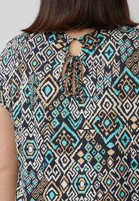 Zwarte top met een patroon van geometrische ontwerpen in turquoise, beige en wit. Details aan de achterkant met een keyhole en een striksluiting. Gladde textuur.