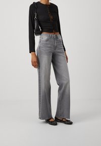 Haut noir à manches longues avec détails de boutons et motif en treillis, associé à un jean gris ample taille haute et des ballerines noires cloutées.