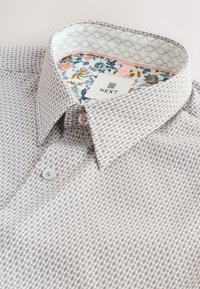 Chemise pour homme à boutons avec un petit motif géométrique gris, col intérieur floral, et étiquette de la marque « Next ».