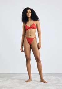 Rode kant lingerie set bestaande uit een bralette met dunne bandjes en een bijpassende string. Zachte, sheer textuur met bloemmotieven.