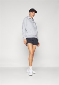 Felpa grigia con cappuccio e lacci, abbinata a pantaloni corti blu navy. Un cappellino nero e scarpe da ginnastica bianche completano il look. Design semplice.