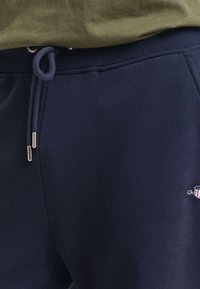 Marineblå joggebukser med en myk tekstur, som har strikk i livet og brodert logo detalj på siden.