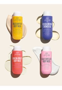 Quatre bouteilles de gel douche Sol de Janeiro aux couleurs vives en jaune, bleu, corail et rose, chacune avec des textures de produit étalées derrière elles.