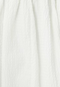 Tessuto bianco con una leggera trama stropicciata, caratterizzato da un aspetto leggero e arioso. Materiale morbido e leggero, adatto per essere drappeggiato.