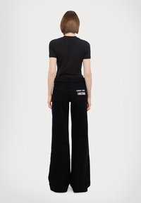 Black fitted t-shirt paired with wide-leg black jeans featuring a bold "COUTURE" graphic on the back pocket. Smooth texture, casual design.