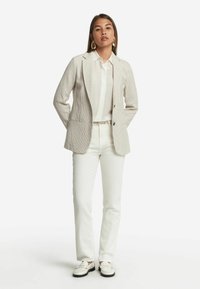 Blazer i ljus beige med ett strukturerat mönster, vit skjorta, krämfärgade byxor och vita loafers. Har slag med snitt och enkel knappstängning.