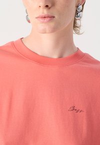 Coral cotton t-shirt with a crew neck and short sleeves, featuring a small black "BOSS" logo on the left chest area. Smooth texture.