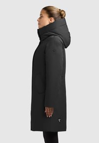 Svart huva parkas med en texturerad yta, sidofickor och en logotypdetalj. Rakt snitt och knälång design.