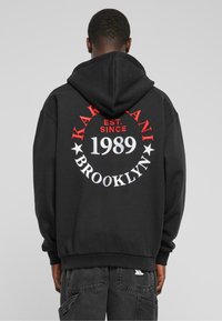 Sudadera con capucha negra con un gráfico circular que presenta "KARAKANI," "BROOKLYN," "EST. SINCE," y "1989" en letras rojas y blancas.