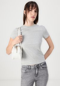 Gray, fitted t-shirt with short sleeves and a round neckline, paired with high-waisted, light gray jeans. White handbag with a zipper detail.
